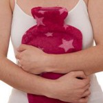 Photo of a woman's hands holdilng a hot water bottle to her abdomen