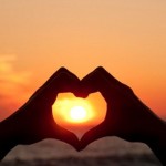 Photo of two hands making a heart shape aroudn the sun