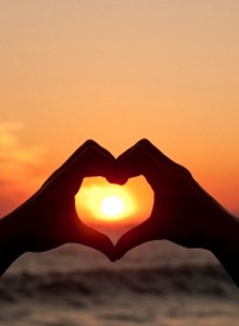 Photo of two hands making a heart shape aroudn the sun