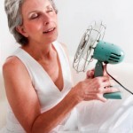 Photo of an older woman cooling herself off with a fan
