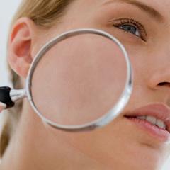 Photo of a woman holding a magnifying glass up to her skin