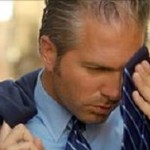 Photo of a sweating man wiping his face with his tie