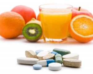 Photo of vitamins in foreground and fresh fruit in the background