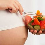 Photo of a woman's pregnant belly and bowl of fruit salad