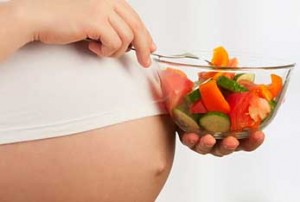Photo of a woman's pregnant belly and bowl of fruit salad