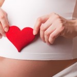 Photo of a pregnant belly with woman holding a red heart over it