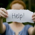 Depressed woman holding up a 'help' sign